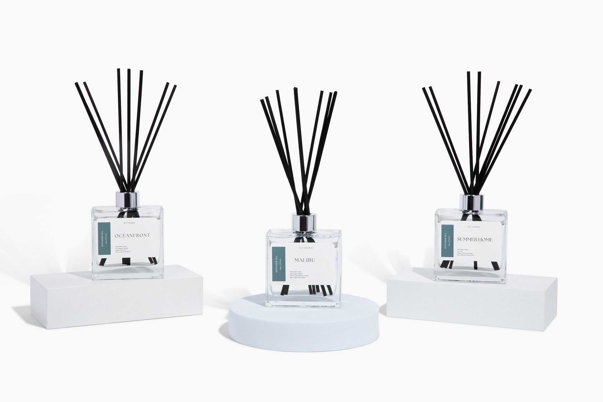 Three diffusers with reeds on white stands against a white background
